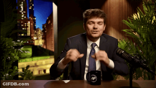A Man In A Suit And Tie Sitting In Front Of A Microphone With A Mug That Says Af GIF