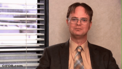 A Man In A Suit And Tie Sitting In Front Of A Window With Blinds GIF