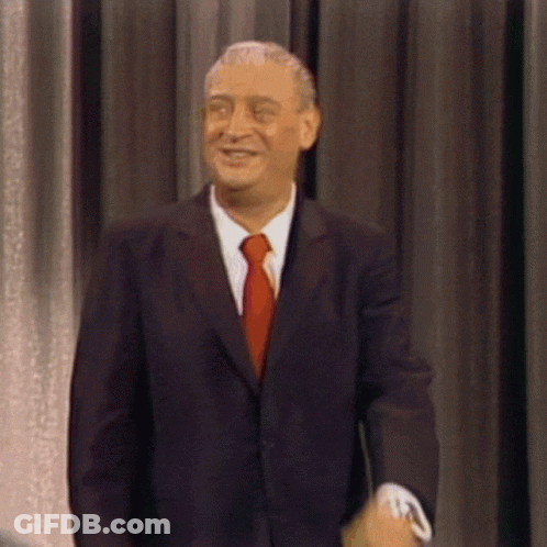 A Man In A Suit And Tie Smiles While Standing In Front Of A Curtain GIF