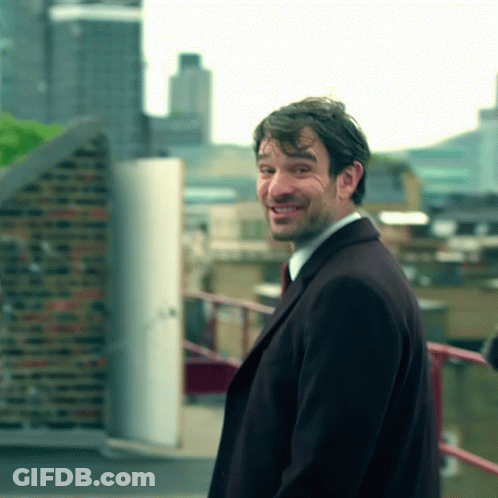 A Man In A Suit And Tie Smiles While Standing On A Balcony GIF
