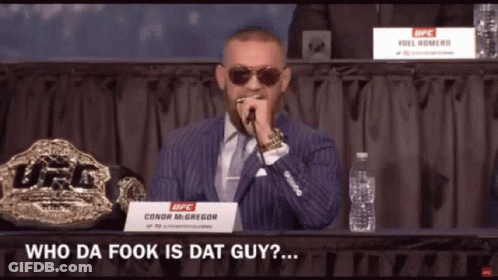 A Man In A Suit And Tie Speaking Into A Microphone With A Sign That Says Conor Mcgregor On It GIF