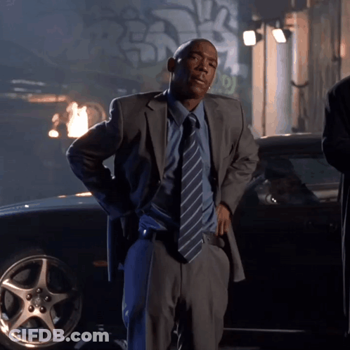 A Man In A Suit And Tie Standing In Front Of A Car GIF