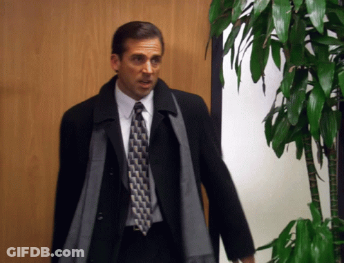 A Man In A Suit And Tie Standing In Front Of A Plant GIF