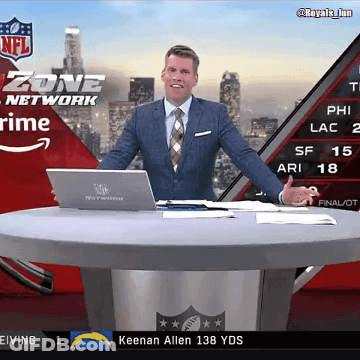 A Man In A Suit And Tie Stands At A Table With A Laptop In Front Of A Screen That Says Zone Network GIF