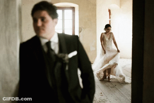 A Man In A Suit And Tie Stands Behind A Bride In A Wedding Dress GIF