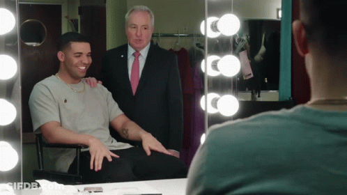 A Man In A Suit And Tie Stands Behind A Man In A Chair GIF