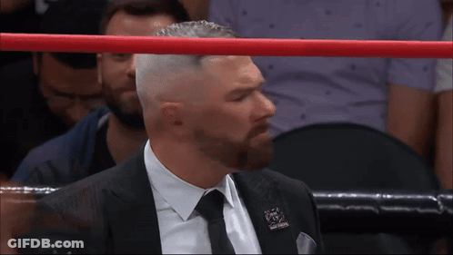 A Man In A Suit And Tie Stands In A Boxing Ring With A Red Rope GIF