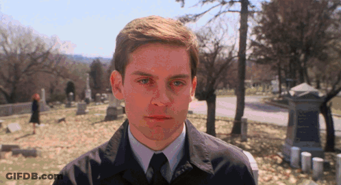 A Man In A Suit And Tie Stands In A Cemetery Looking At The Camera GIF