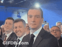 A Man In A Suit And Tie Stands In A Crowd GIF