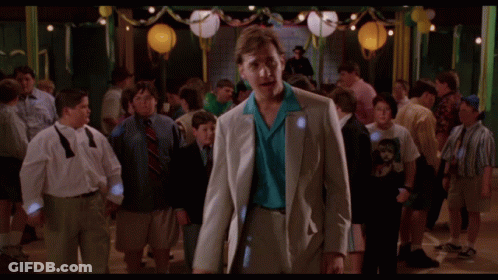A Man In A Suit And Tie Stands In A Crowd Of People At A Party GIF