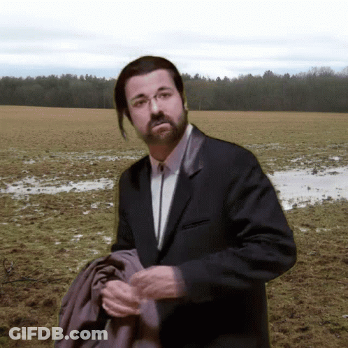 A Man In A Suit And Tie Stands In A Field GIF