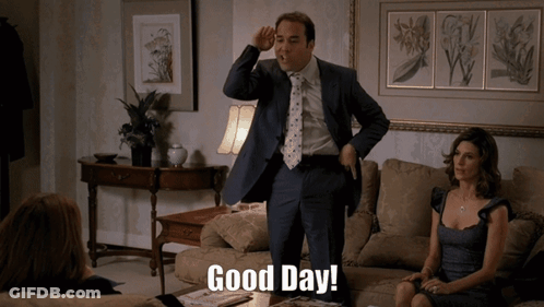 A Man In A Suit And Tie Stands In A Living Room And Says Good Day GIF