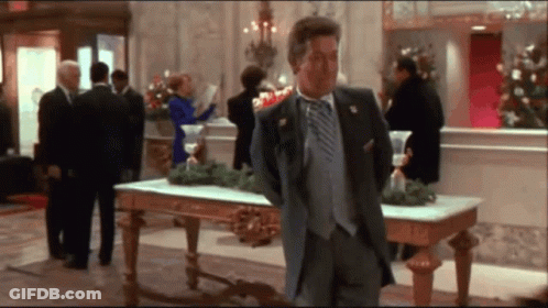 A Man In A Suit And Tie Stands In A Lobby GIF