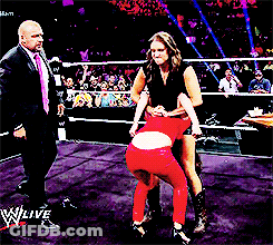 A Man In A Suit And Tie Stands In A Wrestling Ring Watching A Woman In Red Tights GIF