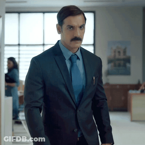 A Man In A Suit And Tie Stands In An Office GIF