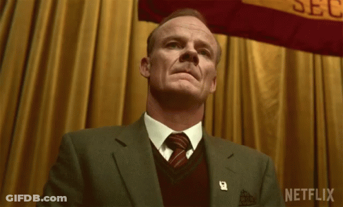A Man In A Suit And Tie Stands In Front Of A Banner That Says Netflix GIF