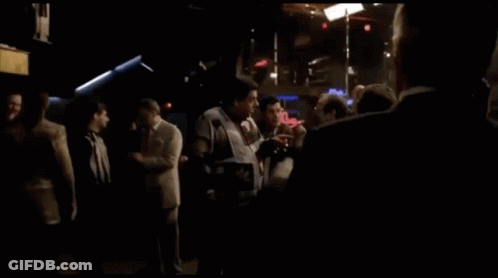 A Man In A Suit And Tie Stands In Front Of A Budweiser Sign GIF