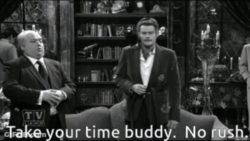 A Man In A Suit And Tie Stands In Front Of A Couch With The Words Take Your Time Buddy No Rush Below Him GIF