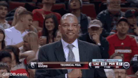 A Man In A Suit And Tie Stands In Front Of A Crowd At A Basketball Game With Technical Foul Written On The Screen GIF