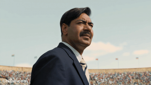 A Man In A Suit And Tie Stands In Front Of A Crowd In A Stadium GIF