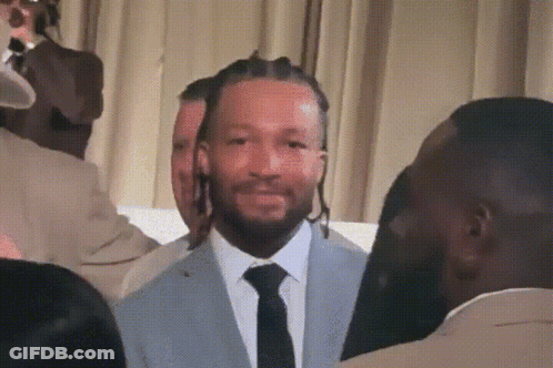 A Man In A Suit And Tie Stands In Front Of A Crowd GIF
