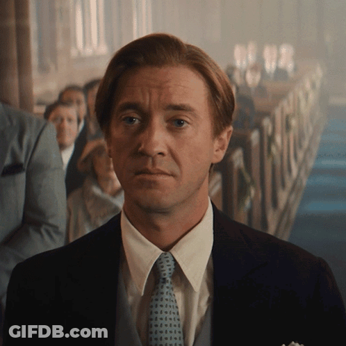 A Man In A Suit And Tie Stands In Front Of A Crowd Of People GIF
