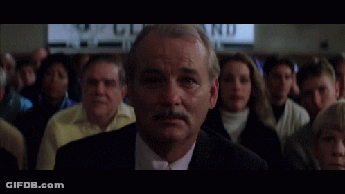 A Man In A Suit And Tie Stands In Front Of A Crowd With A Sign In The Background That Says " Wd " GIF