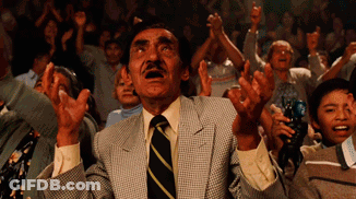A Man In A Suit And Tie Stands In Front Of A Crowd With His Hands In The Air GIF