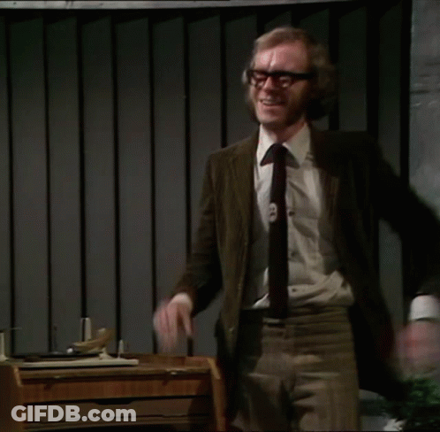 A Man In A Suit And Tie Stands In Front Of A Desk With His Arms Outstretched GIF