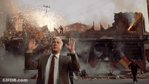 A Man In A Suit And Tie Stands In Front Of A Destroyed Building GIF