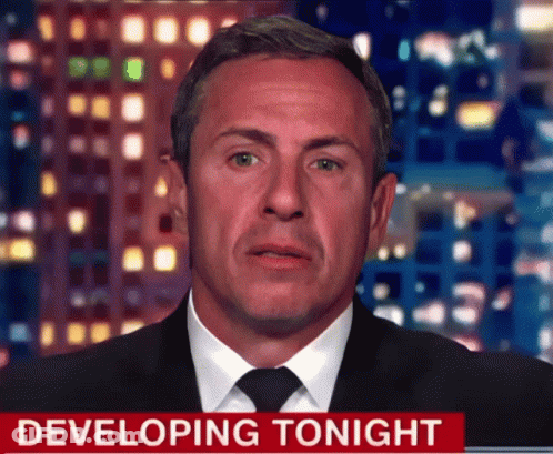 A Man In A Suit And Tie Stands In Front Of A Developing Tonight Sign GIF