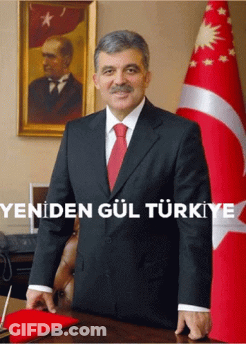 A Man In A Suit And Tie Stands In Front Of A Flag With The Words Yeniden Gul Turkey Written Below Him GIF