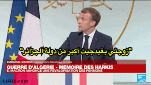 A Man In A Suit And Tie Stands In Front Of A Flag GIF