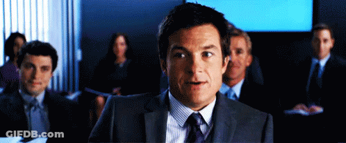 A Man In A Suit And Tie Stands In Front Of A Group Of People In Suits And Ties GIF