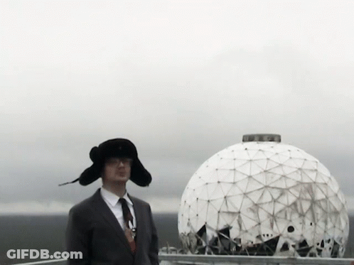 A Man In A Suit And Tie Stands In Front Of A Large White Dome GIF