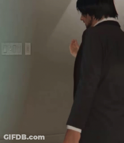 A Man In A Suit And Tie Stands In Front Of A Light Switch GIF