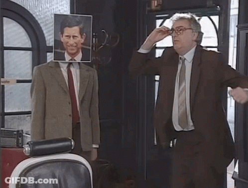 A Man In A Suit And Tie Stands In Front Of A Mannequin With A Picture Of Prince Charles On It GIF