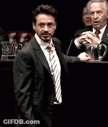 A Man In A Suit And Tie Stands In Front Of A Microphone GIF