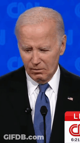 A Man In A Suit And Tie Stands In Front Of A Microphone And A Cnn Logo GIF