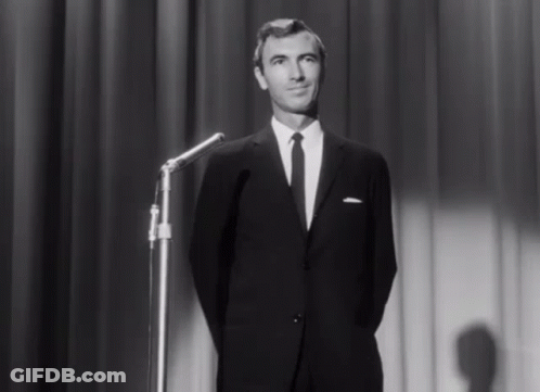A Man In A Suit And Tie Stands In Front Of A Microphone On A Stage GIF