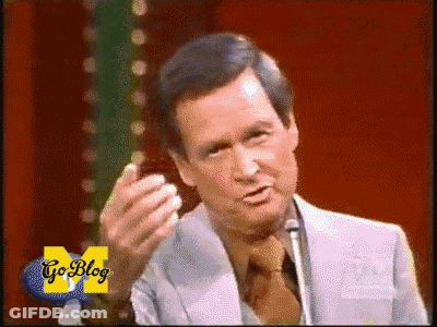 A Man In A Suit And Tie Stands In Front Of A Microphone With Go Blog Written On The Bottom Right GIF