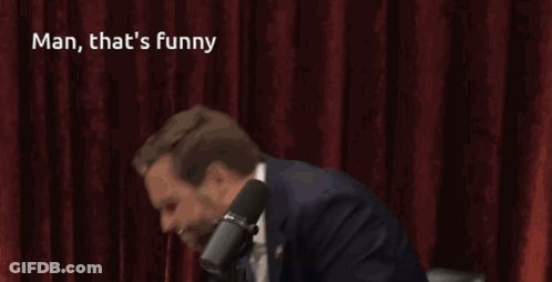 A Man In A Suit And Tie Stands In Front Of A Microphone With The Caption Man That 'S Funny GIF