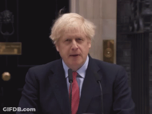 A Man In A Suit And Tie Stands In Front Of A Microphone With The Words An Unexpected Written Below Him GIF