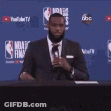 A Man In A Suit And Tie Stands In Front Of A Nba Finals Sign GIF