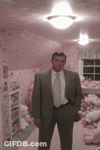 A Man In A Suit And Tie Stands In Front Of A Pink Hello Kitty Room GIF