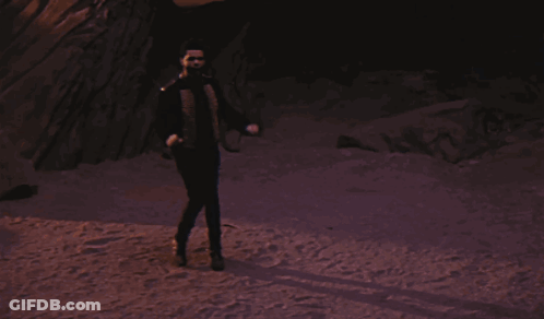 A Man In A Suit And Tie Stands In Front Of A Rock Formation GIF
