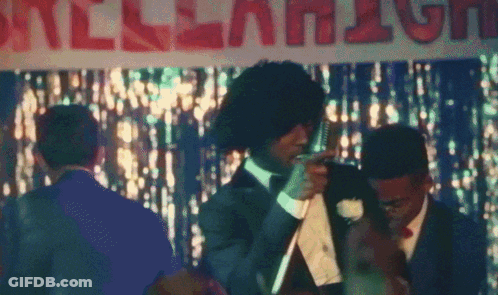 A Man In A Suit And Tie Stands In Front Of A Sign That Says " All-American " GIF