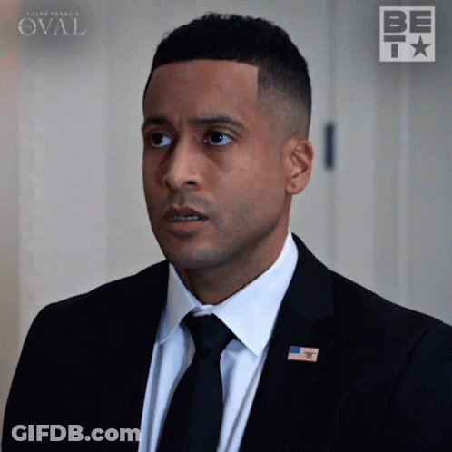 Man In Suit And Tie Standing In Front Of Be Sign GIF