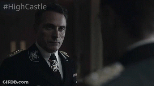 A Man In A Suit And Tie Stands In Front Of A Sign That Says #Highcastle On It GIF