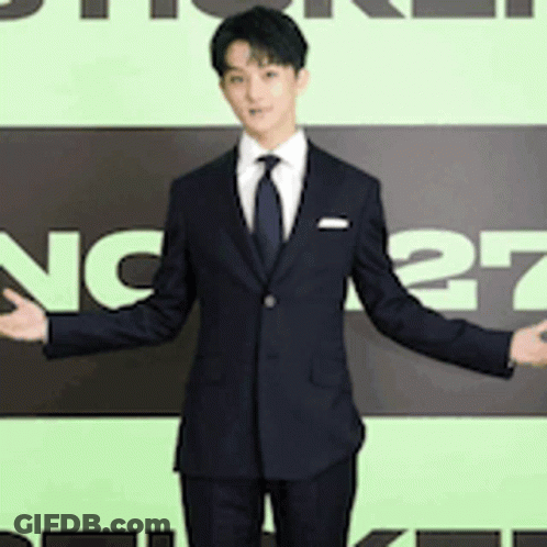 A Man In A Suit And Tie Stands In Front Of A Sign That Says Nc27 GIF